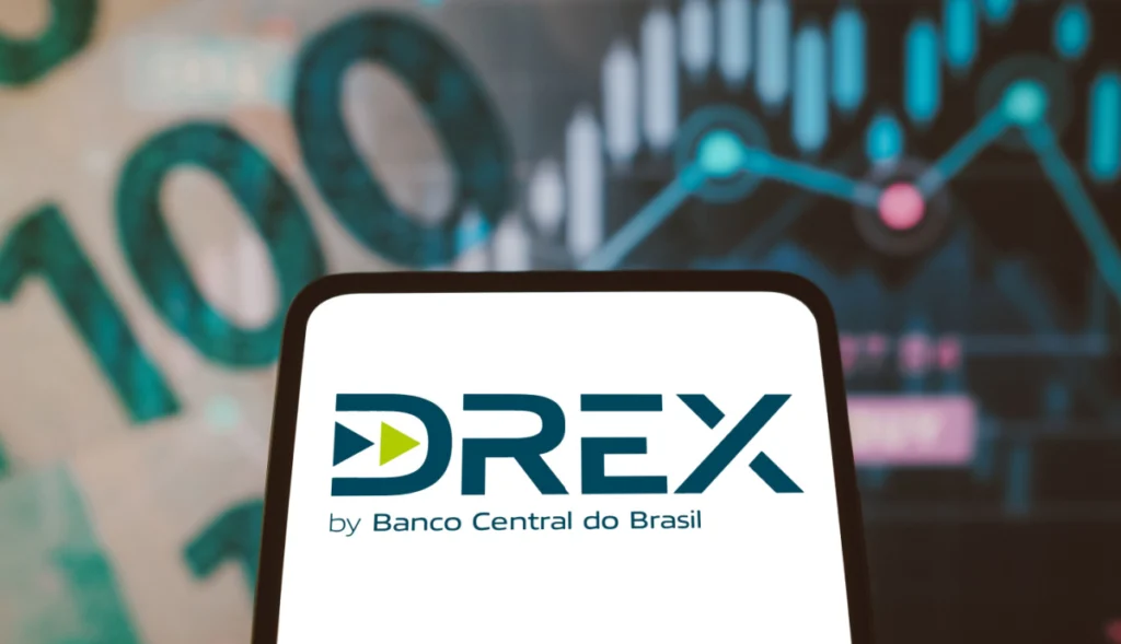 Logo da DREX, a moeda digital brasileira, exibido na tela de um smartphone com um fundo desfocado de gráficos e notas da moeda.