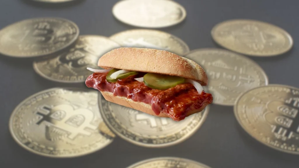 Sanduíche estilo McRib em destaque sobre várias moedas de Bitcoin desfocadas ao fundo, em imagem humorística sobre cripto